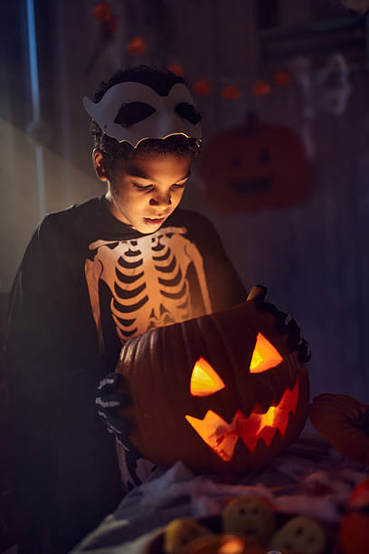 istock African American boy looking inside of Jack O' Lantern at home. 2234431621