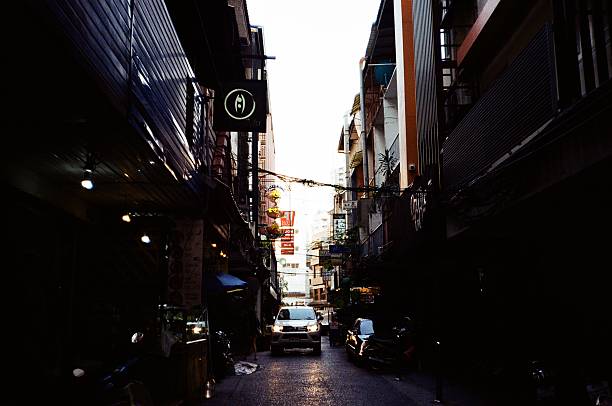 At dusk, a car is driving down a narrow alley