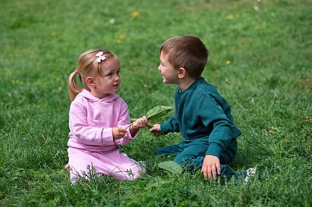 Little brother and sister sitting on the grass in the meadow