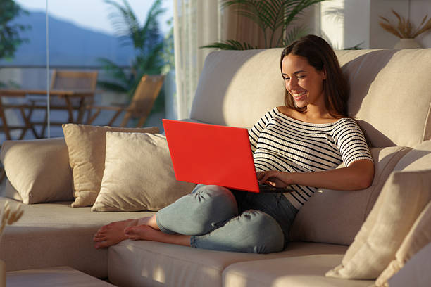 istock Happy woman at home at sunset using red laptop on a sofa 2234440416