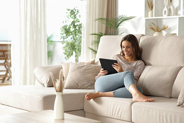 istock Happy woman sitting on a couch using digital tablet at home 2234440911