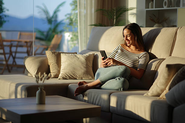 istock Happy woman using mobile phone sitting on a sofa in a house 2234441059