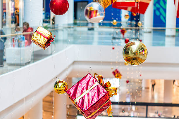 istock Three-dimensional Christmas installation in shopping mall or public area, featuring spherical baubles and gift boxes in pink and red, adorned ceiling, architectural structure visible, bright lighting 2234443598