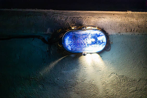 Wall-mounted blue light fixture casting soft glow on dark area, rough textured wall with duct, interplay of light and shadow a