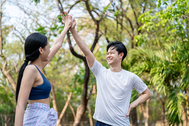 istock Asian young couple making high five while exercise outdoors in garden. Attractive man and woman resting and taking a break while practice workout for health care in park during sunrise after wake up. 2234447879