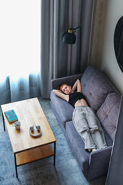 istock Peaceful home atmosphere with woman resting on sofa, morning light through curtains. 2234449200
