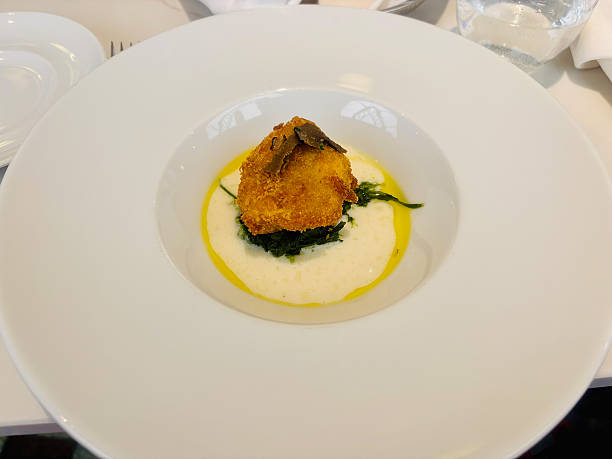 istock Minimalist gourmet dish served on a large white plate, featuring a breaded and fried croquette placed on a bed of sautéed greens 2234454145