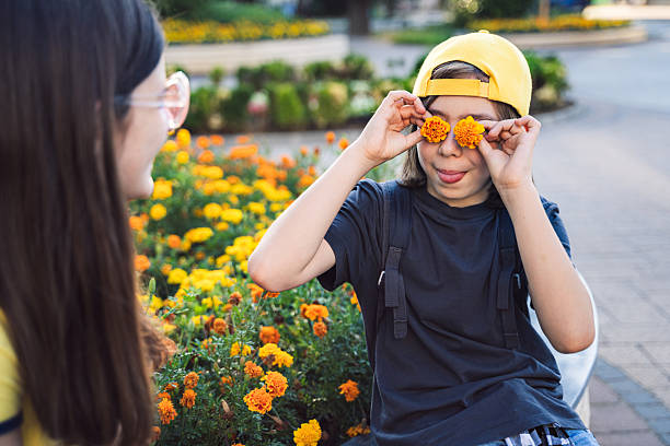 A joyful boy is playing with marigold flowers, placing them on his eyes while enjoying a sunny day in a vibrant garden, showcasing happiness and creativity in nature.