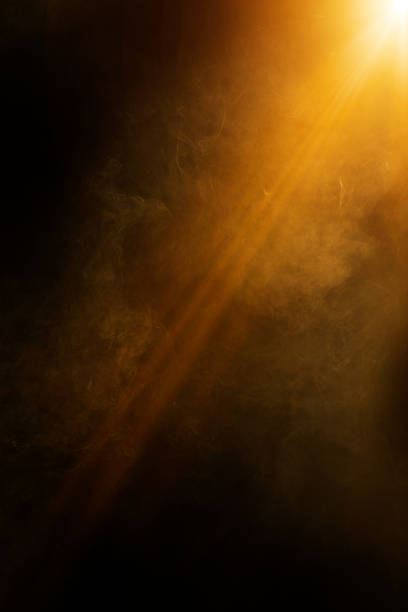 Golden light beam shining through dark smoke or fog