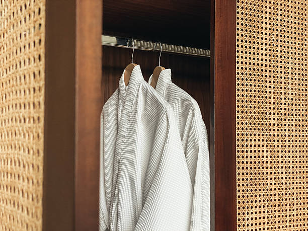 istock Two white clean bathrobes hanging in wooden wardrobe 2234462618