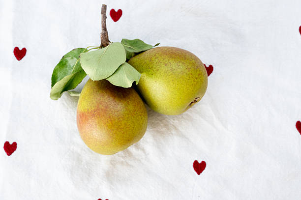 There are two pears placed on a white cloth adorned with red hearts