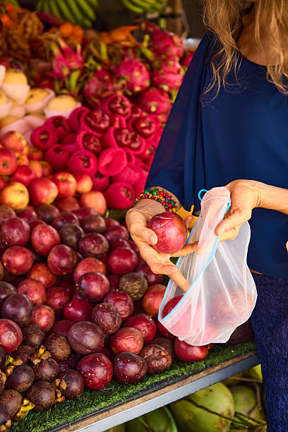 Woman selecting fresh fruit at vibrant farmers market with eco-friendly bag