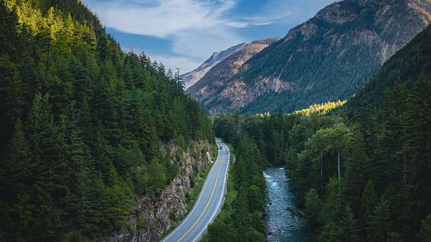 Aerial view of a scenic road trip along the Sea to Sky Highway (Highway 99) near Lillooet, British Columbia, Canada. The winding mountain road follows a fast-flowing river through dense evergreen forests and rugged peaks. This dramatic landscape captures the essence of Canada travel, freedom, and adventure on one of the country’s most iconic scenic drives.