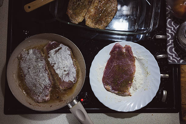 Frying meat rolled in flour on a pan, preparing food at home.