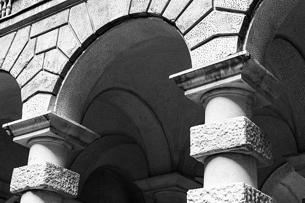 Black and white photograph showcasing detailed stone columns and arches with textured surfaces, highlighting their intricate craftsmanship and historic architectural design