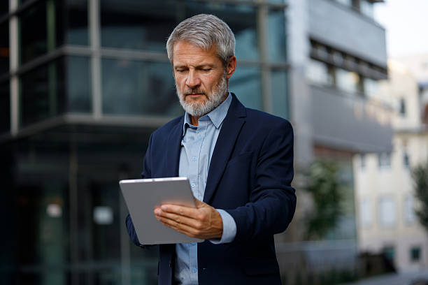 istock Mature businessman reading information on a digital tablet while standing in front of modern office buildings 2234468540