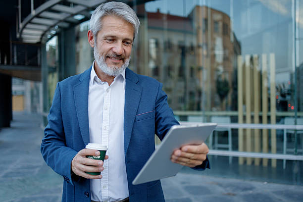 istock Professional businessman working outdoors, smiling while navigating digital tablet and sipping coffee near modern office building 2234471872