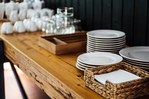 istock Neatly arranged white plates, cups, and glasses on a rustic wooden table, accompanied by a wicker napkin holder, emphasizing simplicity and functional design 2234477465