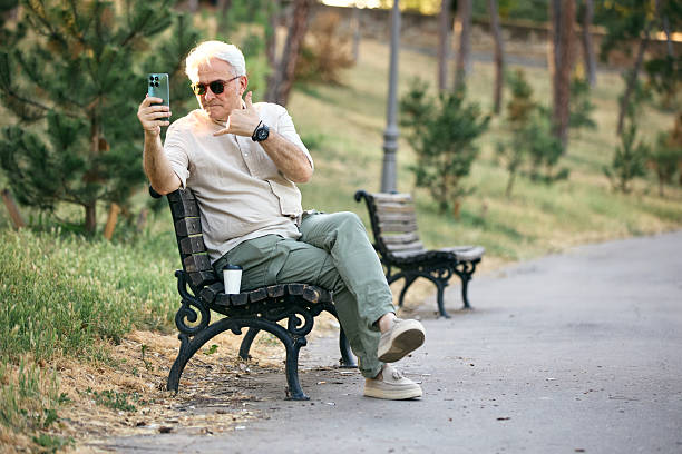 istock Mature Man Relaxing on a Park Bench Using His Smartphone 2234479542