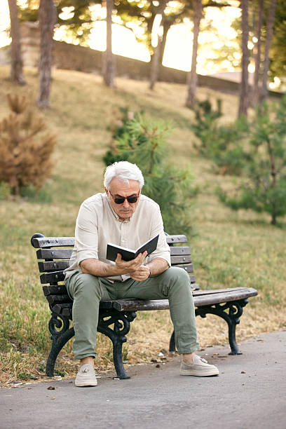 istock Elderly Man Reading a Book on a Park Bench in Autumn 2234479575