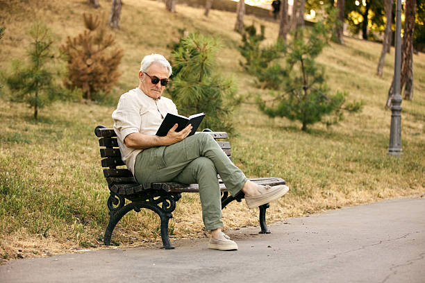 istock Senior Man Reading a Book While Relaxing on a Park Bench 2234479589
