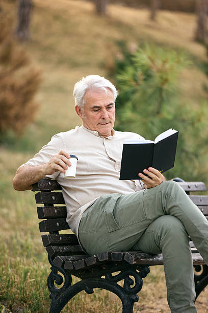 istock Senior Man Relaxing with a Book and Coffee on a Park Bench 2234479626