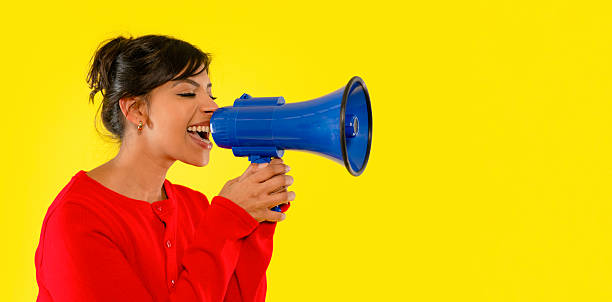 istock Young woman enthusiastically using a blue megaphone in front of a bright yellow background, expressing excitement and energy during her activity 2234482046