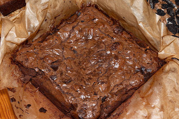 Close up of square homemade chocolate brownie with shiny cracked crust, rich fudgy texture and baked edges, delicious dessert for sweet lovers.