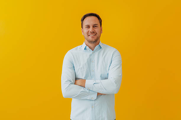 istock Confident businessman in button down shirt poses against bright yellow backdrop, exuding happiness and success 2234491897