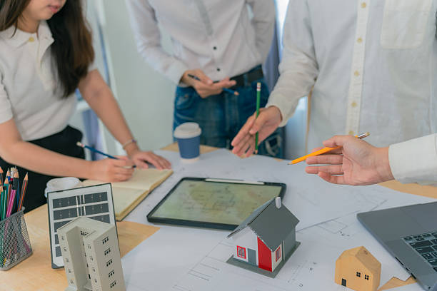 istock Architecture and Construction Concepts - Group of architects with laptop computers meeting with plans on rooftop to plan building design. 2234494340