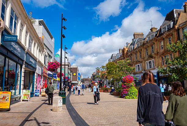 Shoppers in a pedestrianised section of the High Street in Bromley, Kent (Greater London), on a sunny summer day. An old milestone announces that it is “10 Miles to London Bridge”.