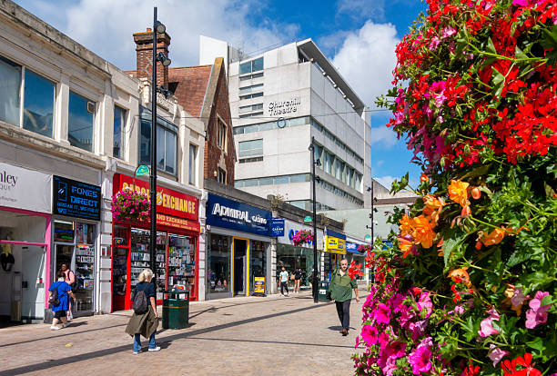 A few shoppers in a pedestrianised section of the High Street in Bromley, Kent (Greater London), on a sunny summer day. Several brightly coloured flower planters enliven the street and Bromley’s famous Churchill Theatre is in the background (named after Sir Winston Churchill who lived at Chartwell, near Westerham, a few miles from Bromley).