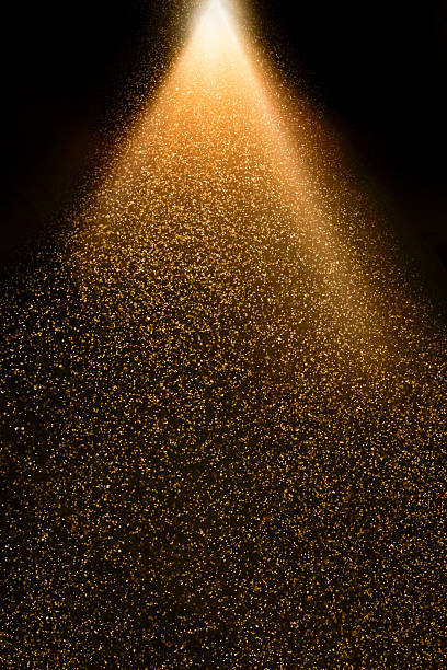istock Golden particles falling from a light beam on black background 2234502548