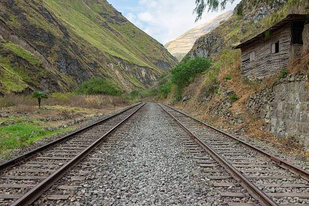 View of old railway tracks leading into a deep mountain valley. The scene evokes a feeling of journey, adventure, and the serene isolation of a secluded natural path.