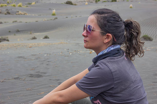 Side profile of a woman with sunglasses, sitting peacefully in a unique desert-like landscape. Her expression is thoughtful and serene, perfect for conveying introspection, travel, and tranquility.