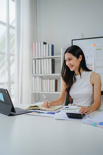 istock Asian businesswoman calculating figures and taking notes while working diligently in a modern office environment, focused on her tasks 2234505748