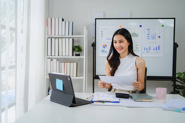 istock Professional asian businesswoman videoconferencing, reviewing documents with confident smile while working remotely from home office 2234505770