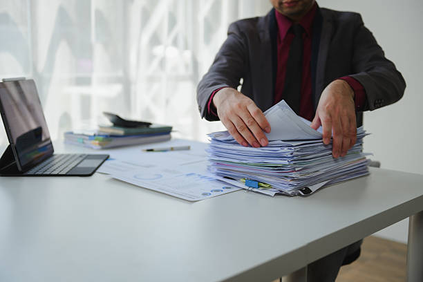 istock Businessman searching through stack of paperwork at office desk with tablet, calculator and financial reports 2234505851