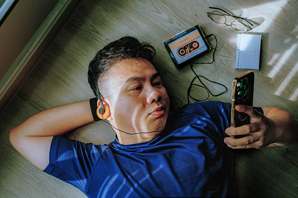 istock Asian Man listening with retro cassette player and headphones while using smartphone 2234508036