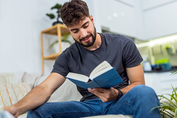istock Young mand relaxes on sofa and reads a book 2234508676