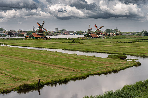 Scenic view of traditional Dutch windmills in Zaandam with changing skies, from calm daylight to approaching rain.