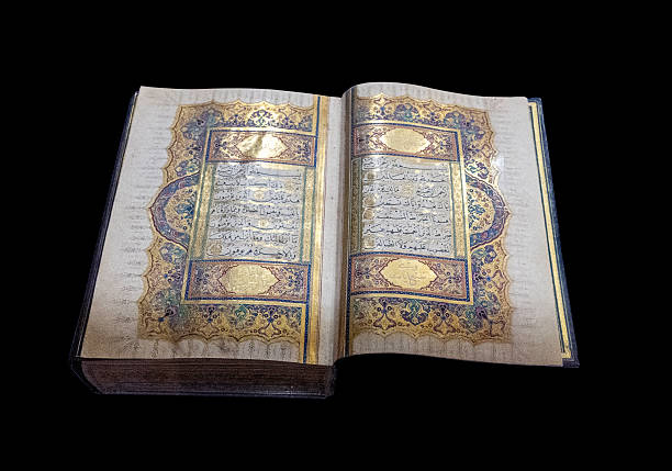 An illuminated Quran manuscript featuring golden and colorful decoration with Arabic calligraphy. The historic Islamic manuscript is displayed open against a black background.