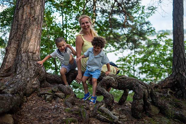 Family enjoying outdoor adventure, mother and children balancing on a fallen log during a forest hike