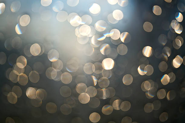 High-resolution abstract background featuring dozens of defocused light circles (bokeh) with subtle prismatic rainbow fringes. The palette blends warm golds and champagne tones with cool grey-blue shadows, creating a gentle gradient from bright upper left to darker lower right. The soft, out-of-focus texture provides abundant copy space for headlines or logos while conveying moods of elegance, celebration, mindfulness, calm, and dreaminess. Ideal for use as a website hero, banner, poster, packaging mockup, invitations, holiday and event graphics, beauty/wellness branding, or luxury marketing. Horizontal orientation; no people, property, or visible trademarks, making it suitable for broad editorial and conceptual commercial applications depending on agency policies.