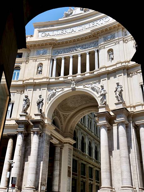 The ornate entrance of the Galleria Umberto I in Naples, Italy, featuring statues and columns. The structure is dramatically framed by a dark archway in the foreground