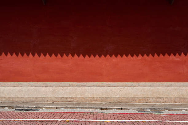 Minimal, graphic close-up of an aged terracotta wall in Tainan, Taiwan—the island’s historic former capital. A dark maroon band along the top casts a sawtooth, zigzag shadow across the sunlit plaster, creating a bold geometric border over warm red–orange gradients and subtle surface textures. The composition is clean and contemporary while still evoking heritage, craftsmanship, and timeless architecture. Ideal as a background for editorial features on travel, culture, and historic districts, or as a striking design texture for posters, web headers, and packaging mockups. Horizontal, full frame; no people and no visible trademarks—appropriate for editorial and conceptual commercial use subject to agency policies.