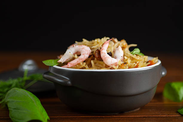 A close-up shot of delicious shrimp fried rice served in eco-friendly disposable paper bowls, highlighting the glossy texture of fresh shrimp and well-cooked rice. This dish features a mix of fluffy rice, scrambled eggs, diced vegetables, and a flavorful seasoning, making it a popular choice in Asian cuisine. The dark background accentuates the rich colors of the ingredients, creating a visually appealing contrast. Ideal for restaurant menus, food delivery services, street food promotions, and culinary-themed designs showcasing traditional seafood dishes.