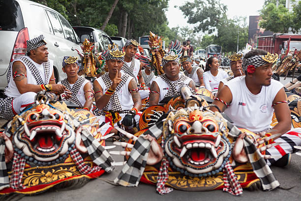 Denpasar, Bali island, Indonesia - June 23, 2018: Young men dressed in ethnic Balinese costumes with Barong, Bona masks before ritual temple procession at street of Denpasar