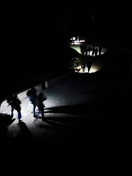 istock Group of people walking in dark illuminated path during nighttime outdoors 2234523403