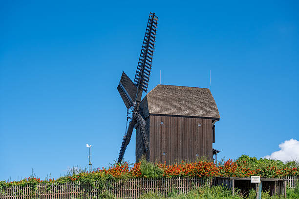 Wooden Windmill with Flowers. A traditional wooden windmill stands on a hill. Bright flowers and clear skies add to the rural beauty.